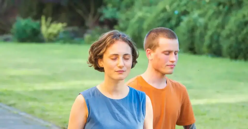 Two people, a young woman and man, eyes closed, peacefully in meditation outdoors