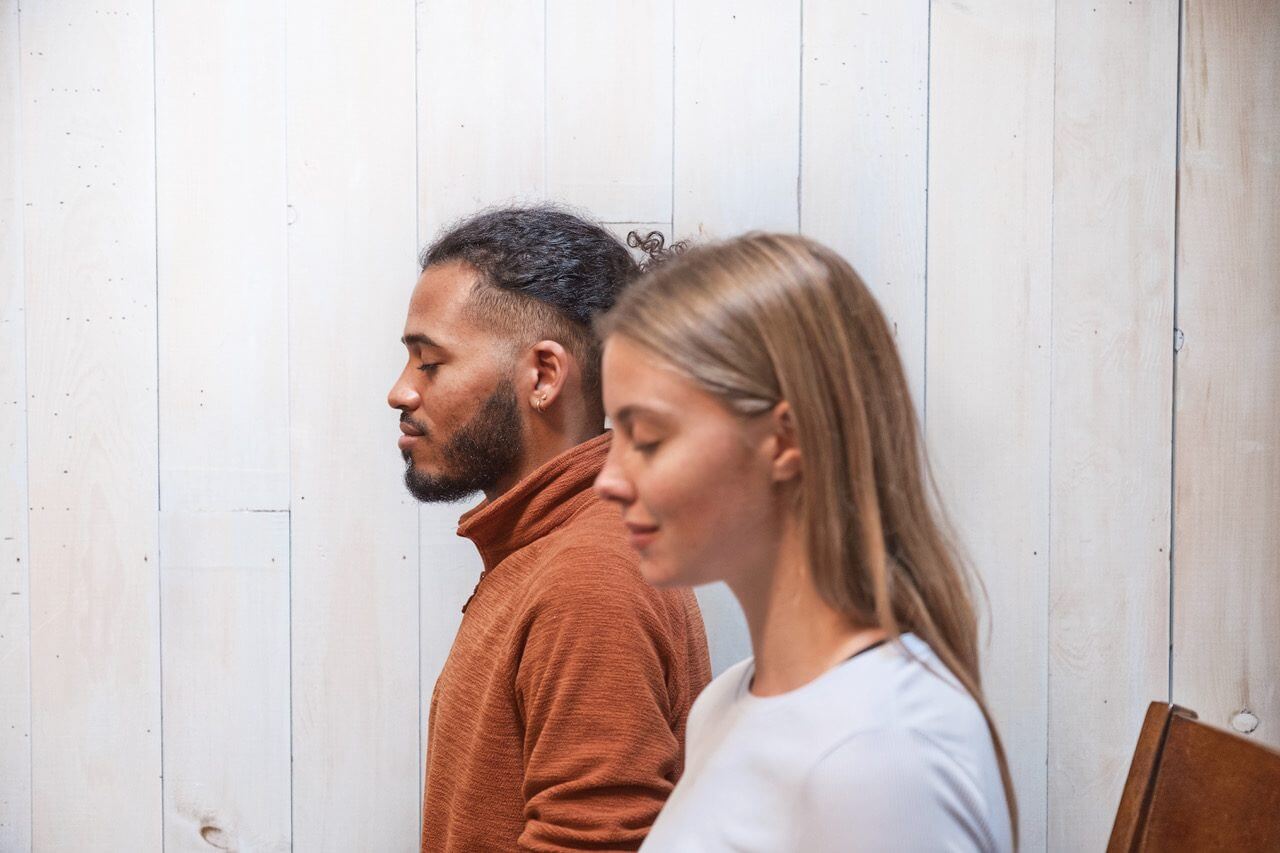 Side on shot of two people, one male, one female engaged in Buddhist meditation together