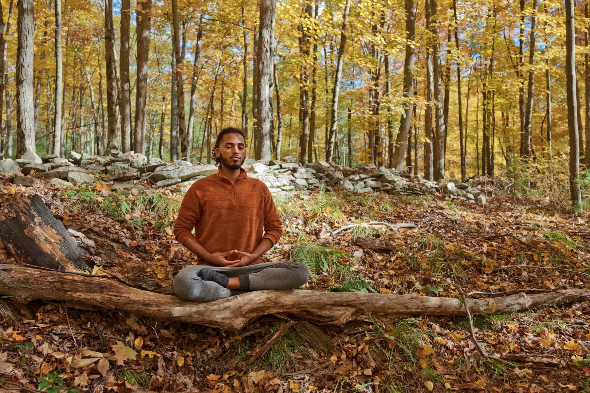 a young man sitting cross-legged and peacefully meditating in the woods
