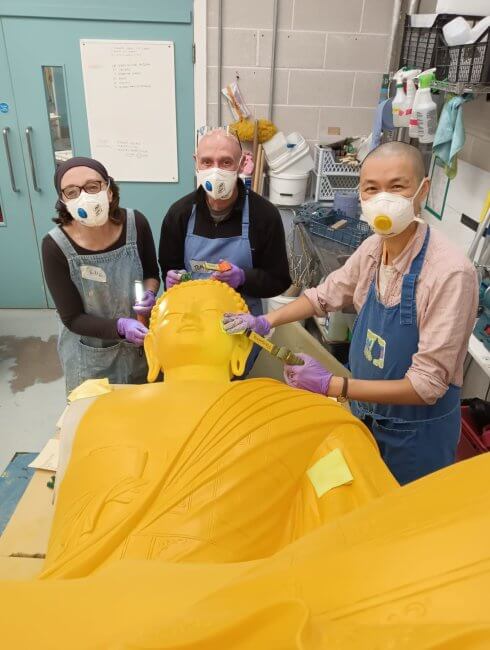 Happy team working on buffing the surface of a serve Buddha statue ready for painting