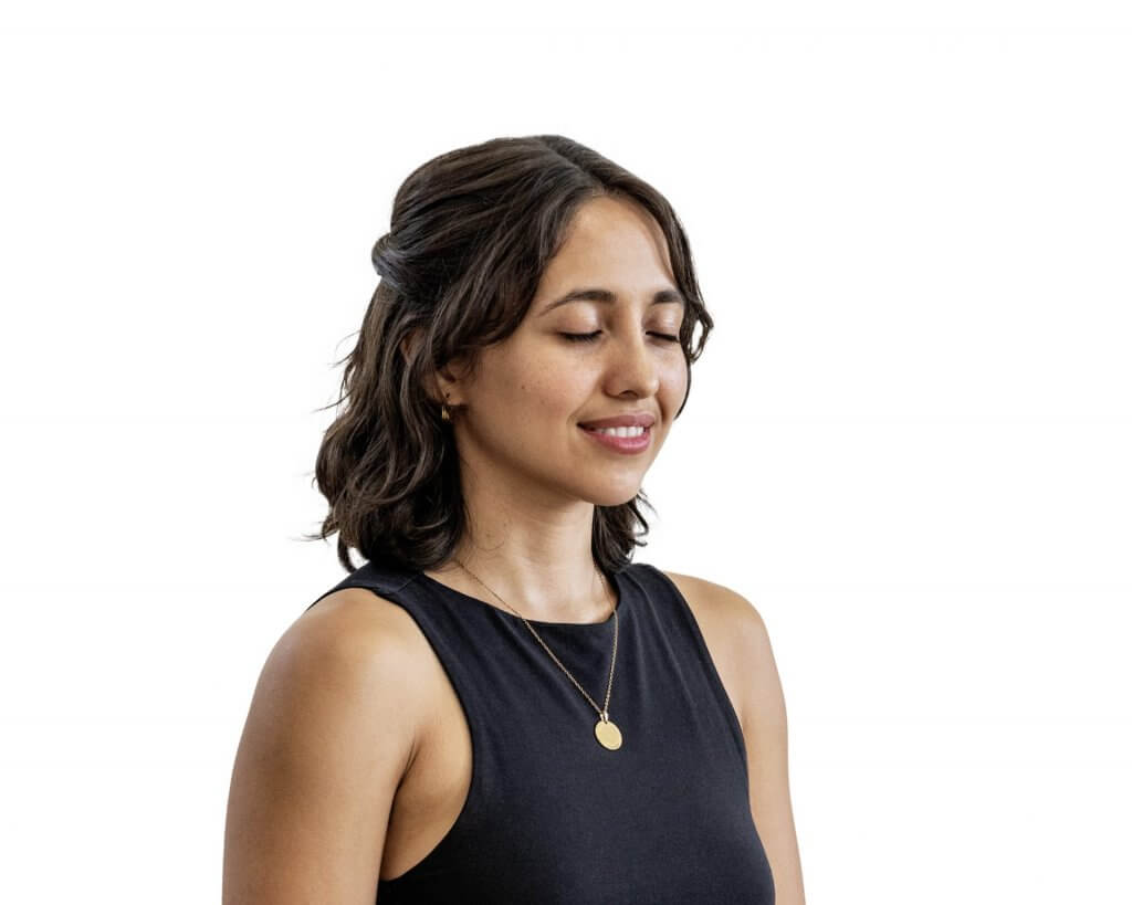 A young woman peacefully meditating with her eyes closed and a gentle smile on her fave
