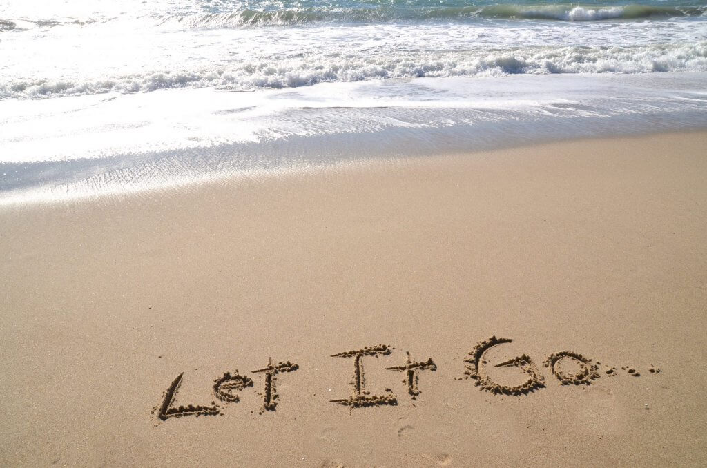 The words "Let it Go" written in sand on a beach